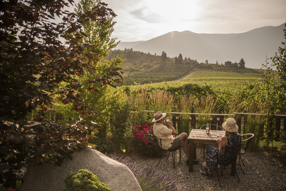 Two people sip wine on a patio looking out at Baillie-Grohman Estate Winery in Creston, BC
