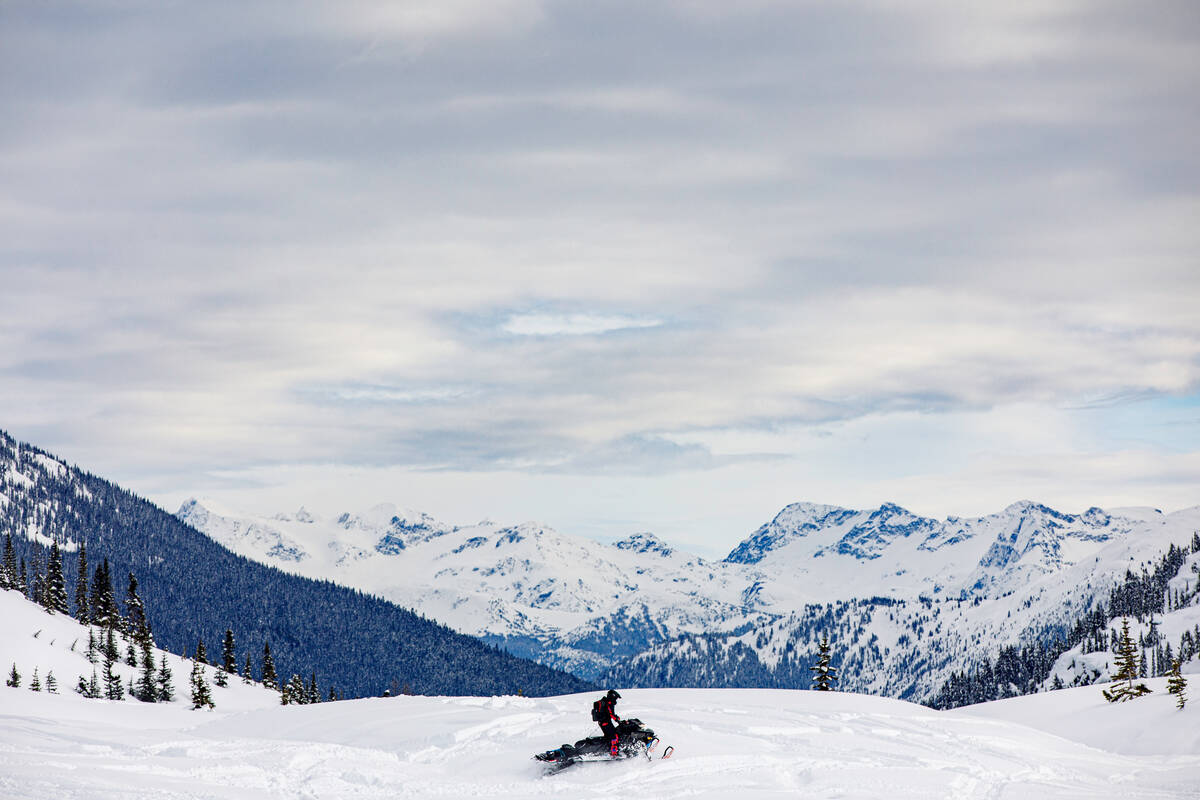 A person on a snowmobile looks out on a snowy, mountainous vista.