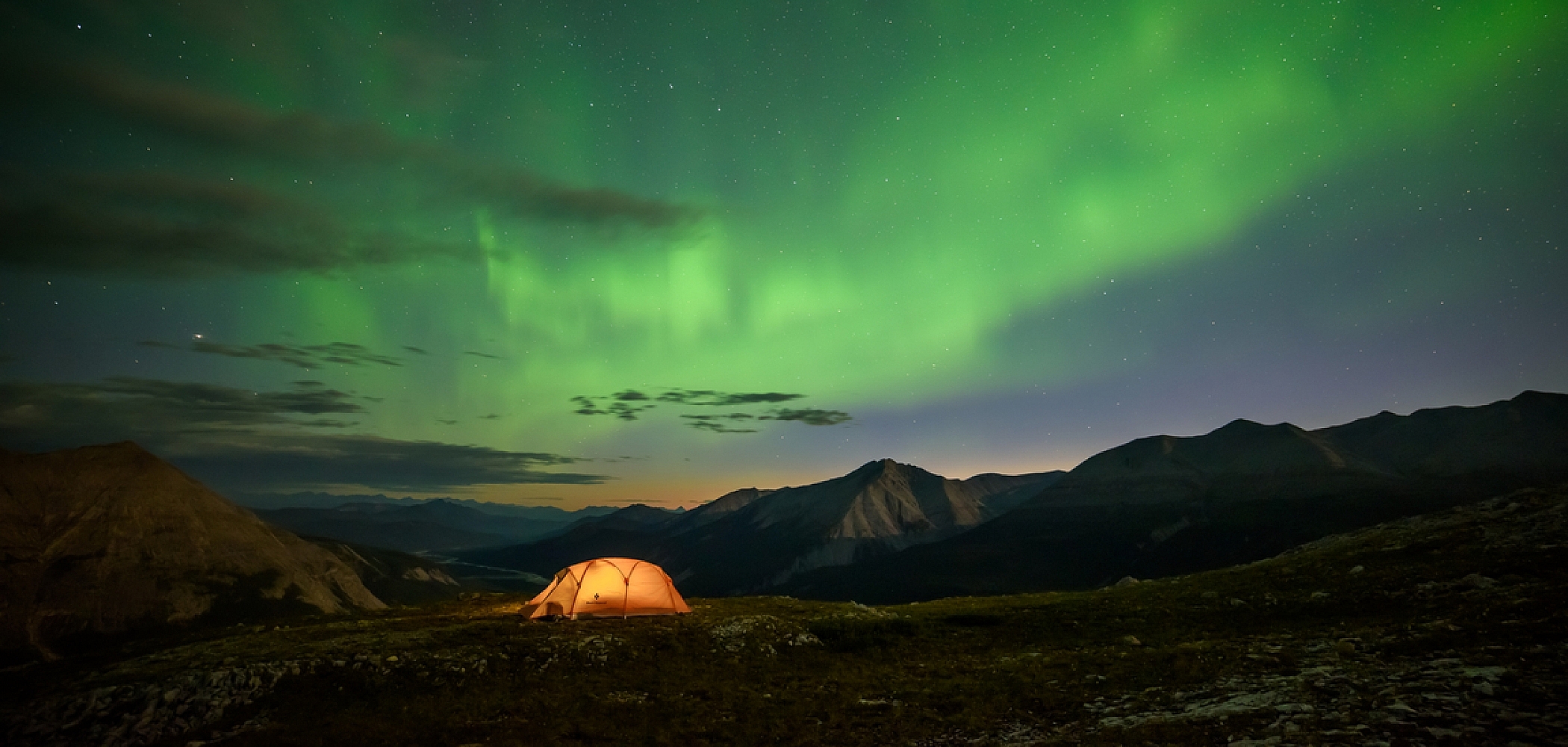 An illuminated tent under the vibrant green Northern Lights.