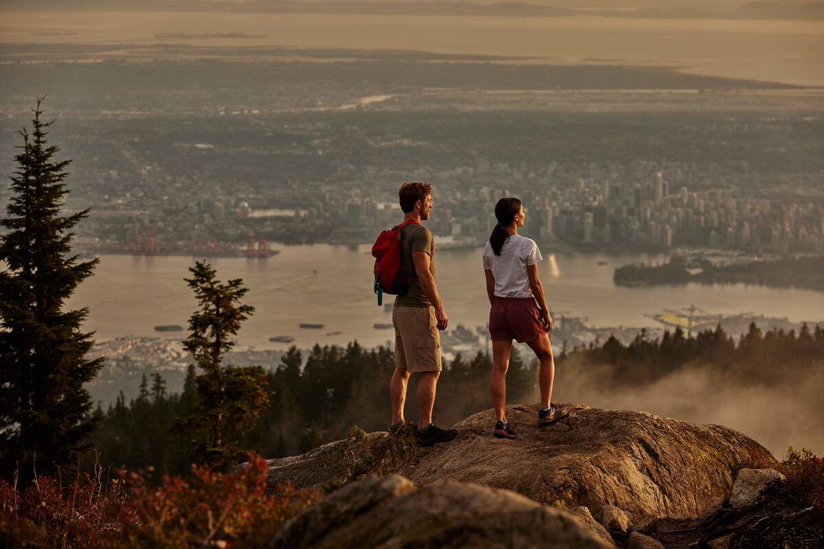 Two hikers look out over Vancouver from a rocky outcropping on Grouse Mountain.