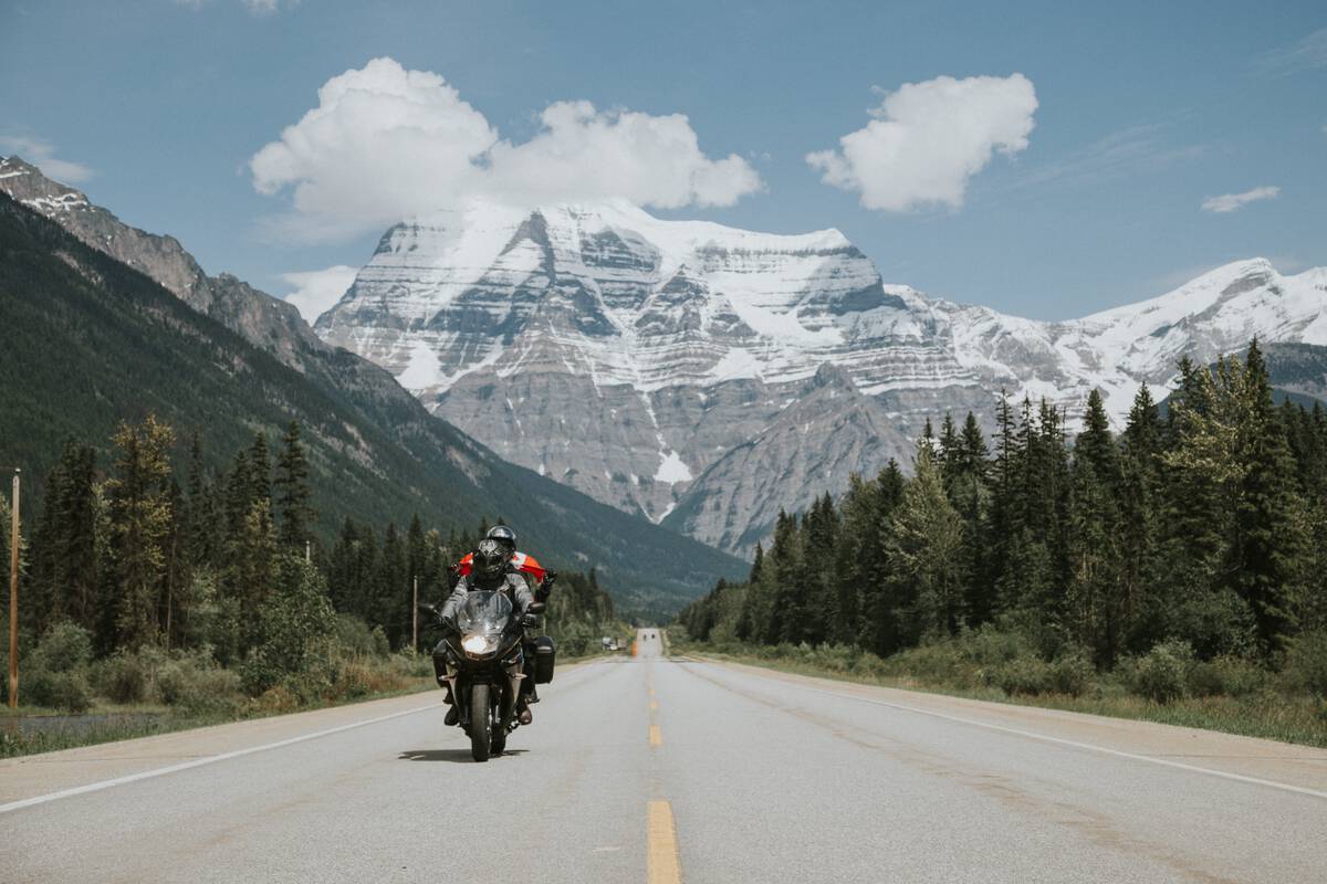 A motorcycle with two people on the highway with imposing Mount Robson in the background.