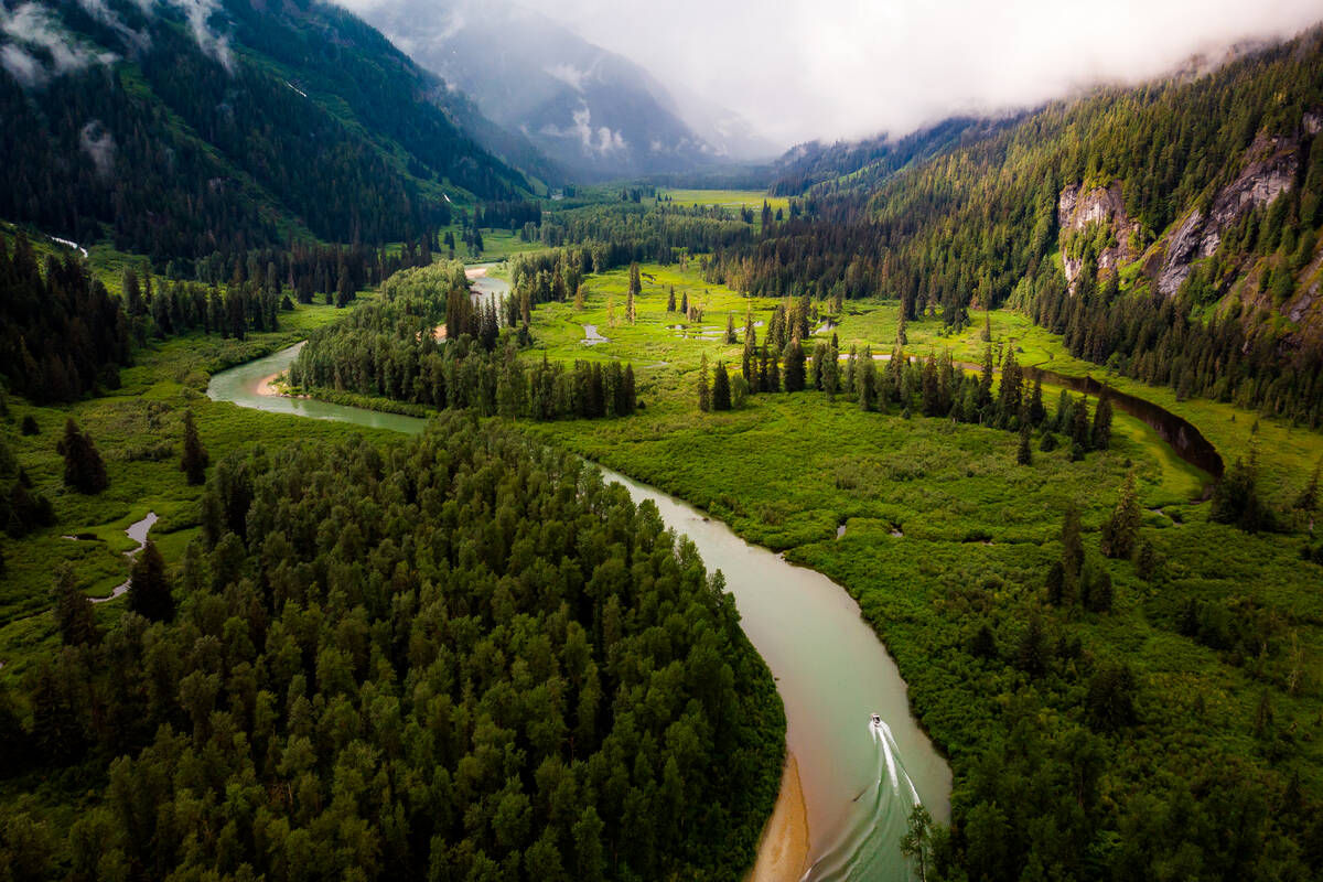 An aerial view of the lush valley surrounded by mountains, with a jet boat cruising up the river.