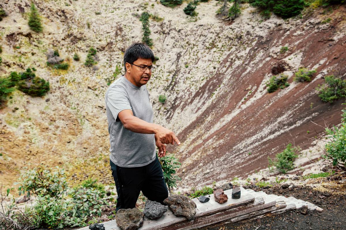 A First Nations guide gives a talk in front of a lava cone, pointing to volcanic rocks.