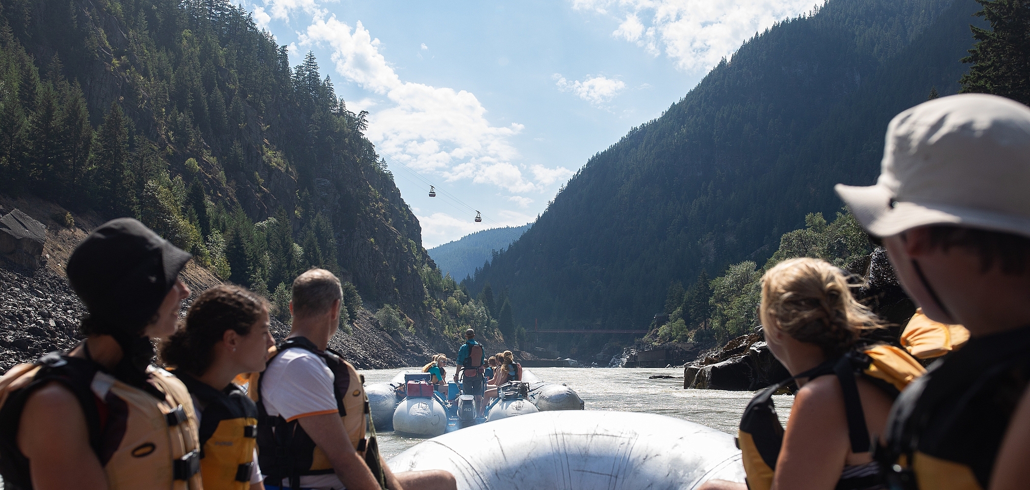 A boat full of rafters float down the Fraser River and are looking up at Hell's Gate.