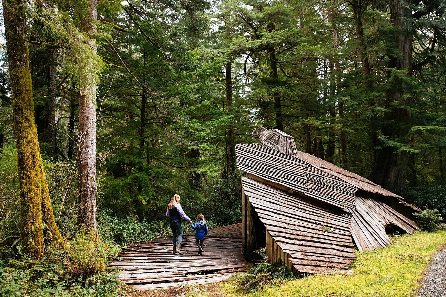 A woman and a young girl walk along a wooden pathway leads to a wooden structure that has the head of an eagle.