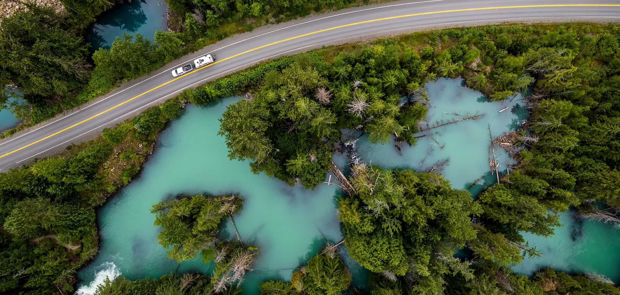 An aerial view of an RV driving through the Drowned Forest, a sea of turquoise water with forest growing into it.