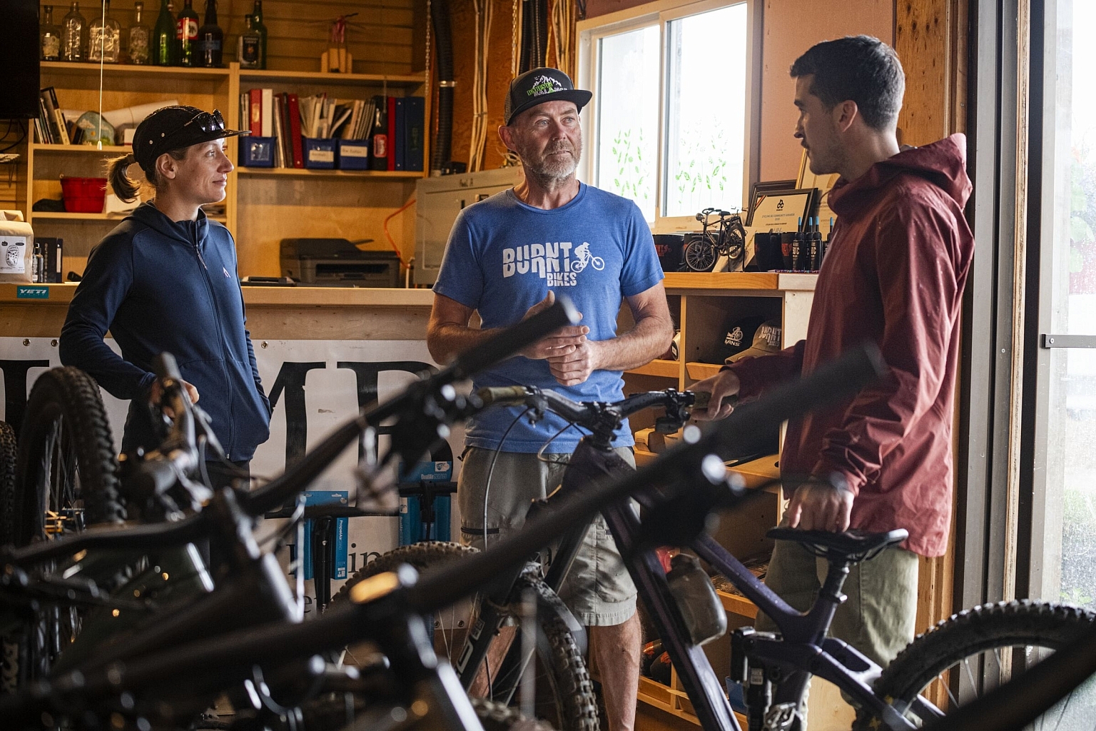 Three people stand inside a bike shop surrounded by bike apparel and gear.