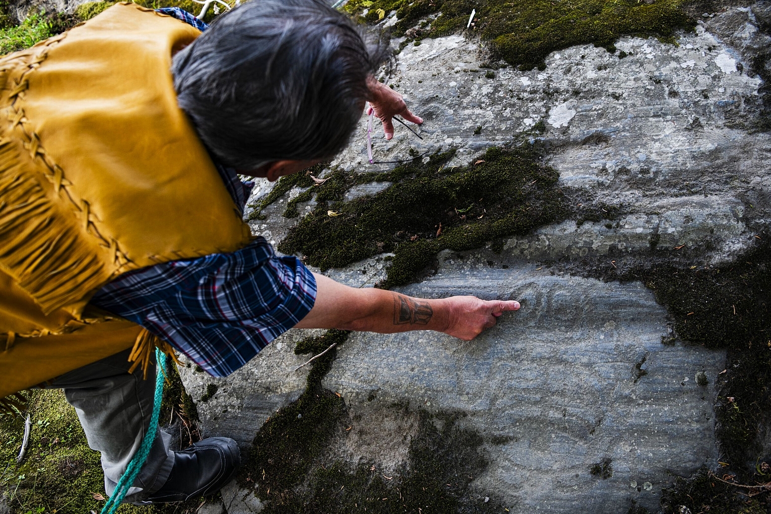 Clyde Anzac of the NIsga'a Nation points to dark rocks containing petroglyphs.