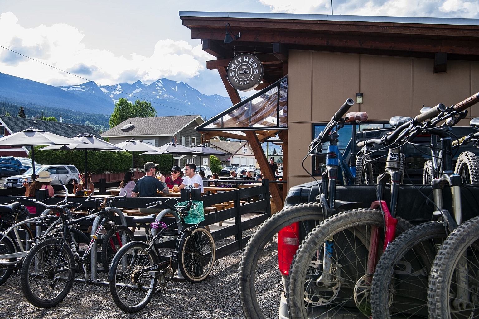 A group of mountain bikers enjoys a patio pint at a local brewery with bikes parked out front.