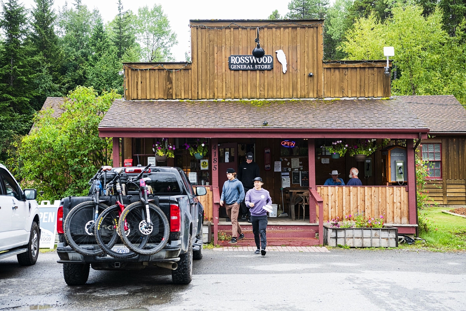 Two people walk out of a general store towards their truck, which is carrying mountain bikes.