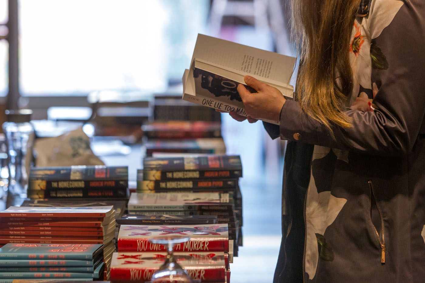 Woman standing and thumbing through a novel at a table full of many different books.