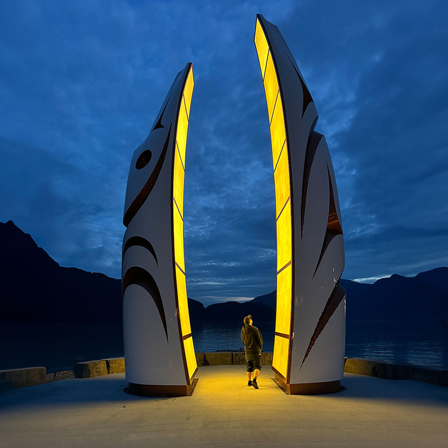 A person walks through the Welcome Gate, all lit up at night with two large carved poles.